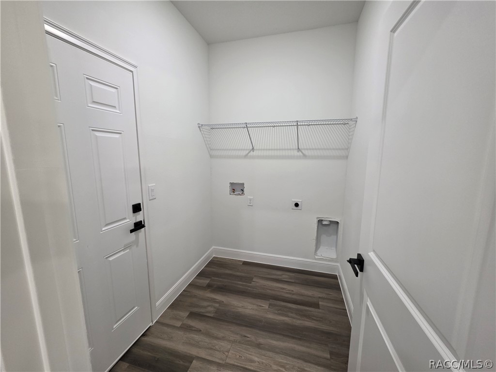 Empty laundry room with a wire shelf, washer and dryer hookups, and dark plank flooring.