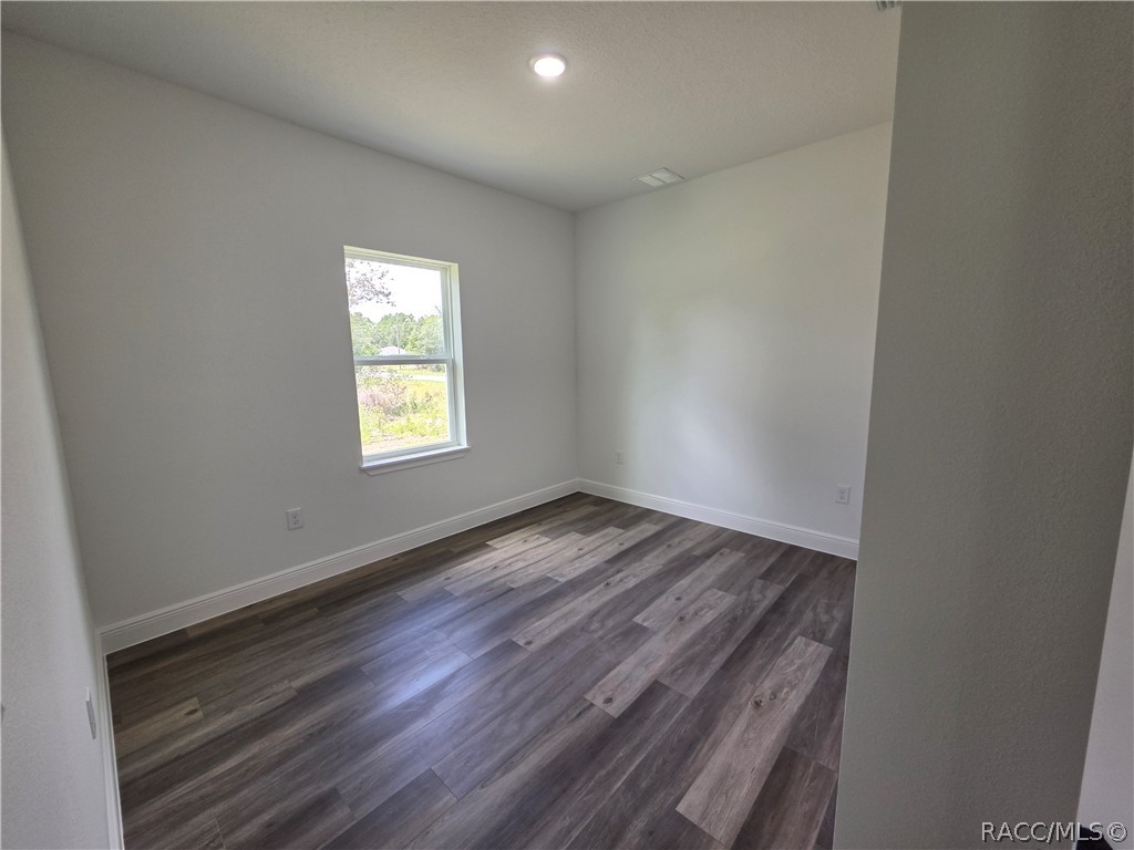 Empty room with dark plank flooring, light gray walls, and a single window.