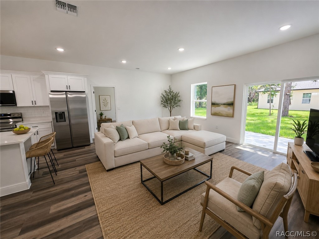 Staged living room with a cream sectional, open white kitchen, and sliding doors to the yard.