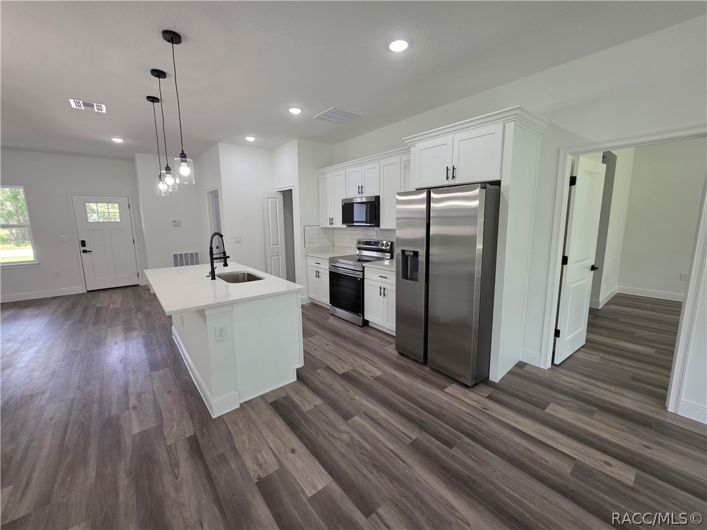 Vacant kitchen with a white island, stainless steel appliances, and gray-brown wood-look flooring.