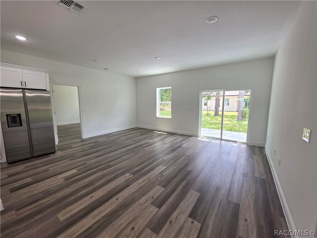 Vacant living area with gray plank flooring, stainless-steel refrigerator, and sliding glass doors to the yard.