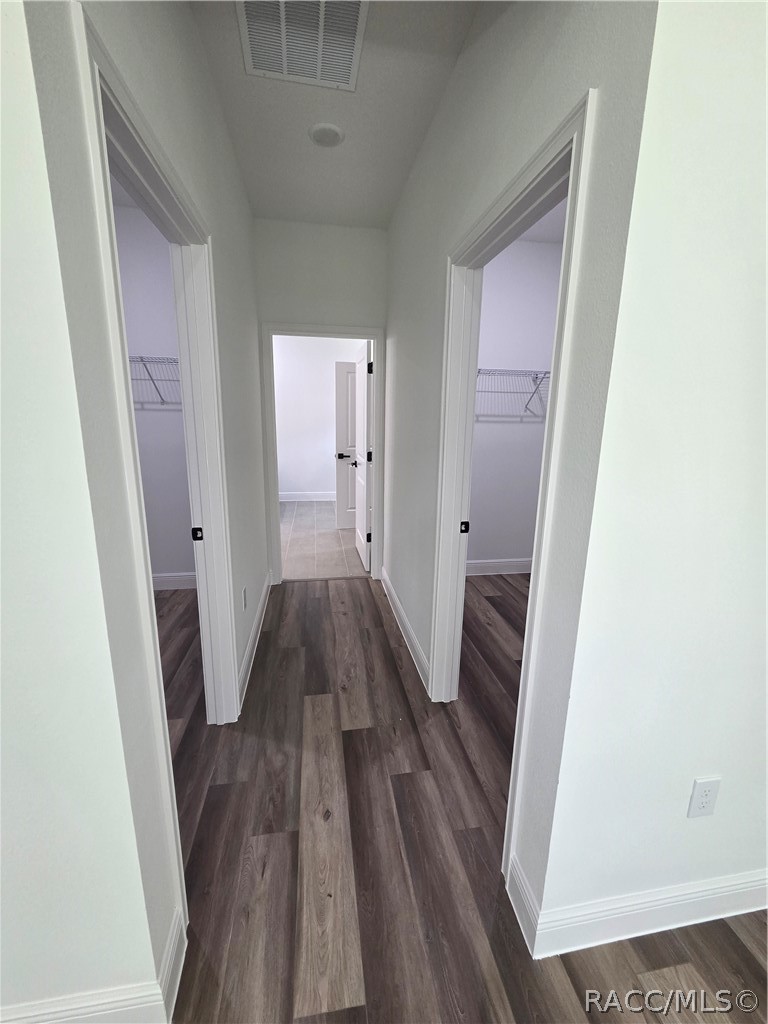 Hallway with dark plank flooring and open closets on both sides.