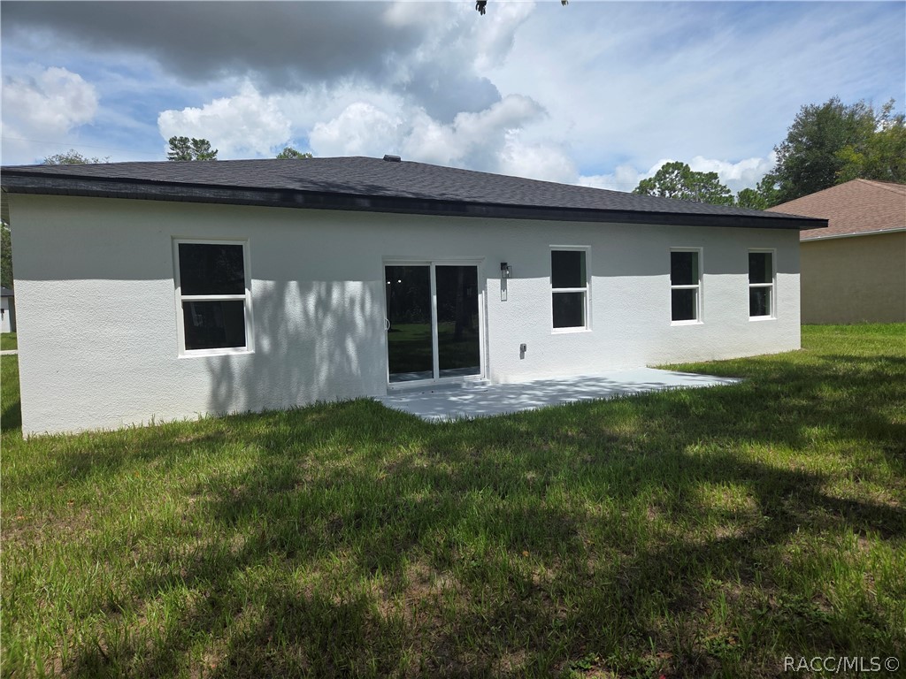 Rear of a white single-story house with a sliding glass door and dark shingle roof.