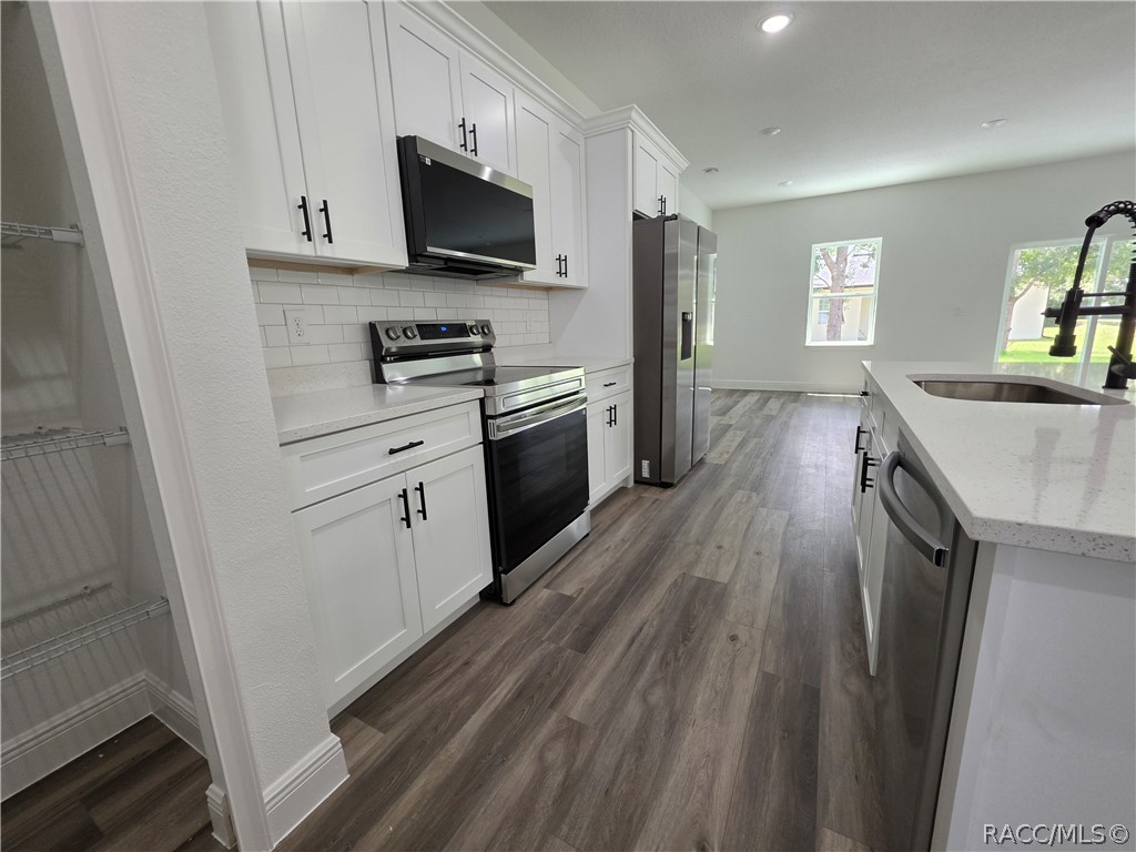 Vacant kitchen with white cabinets, stainless steel appliances, and a large island with sink.