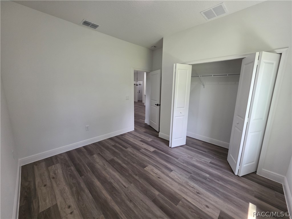 Empty bedroom with gray wood-look flooring and an open double-door closet.