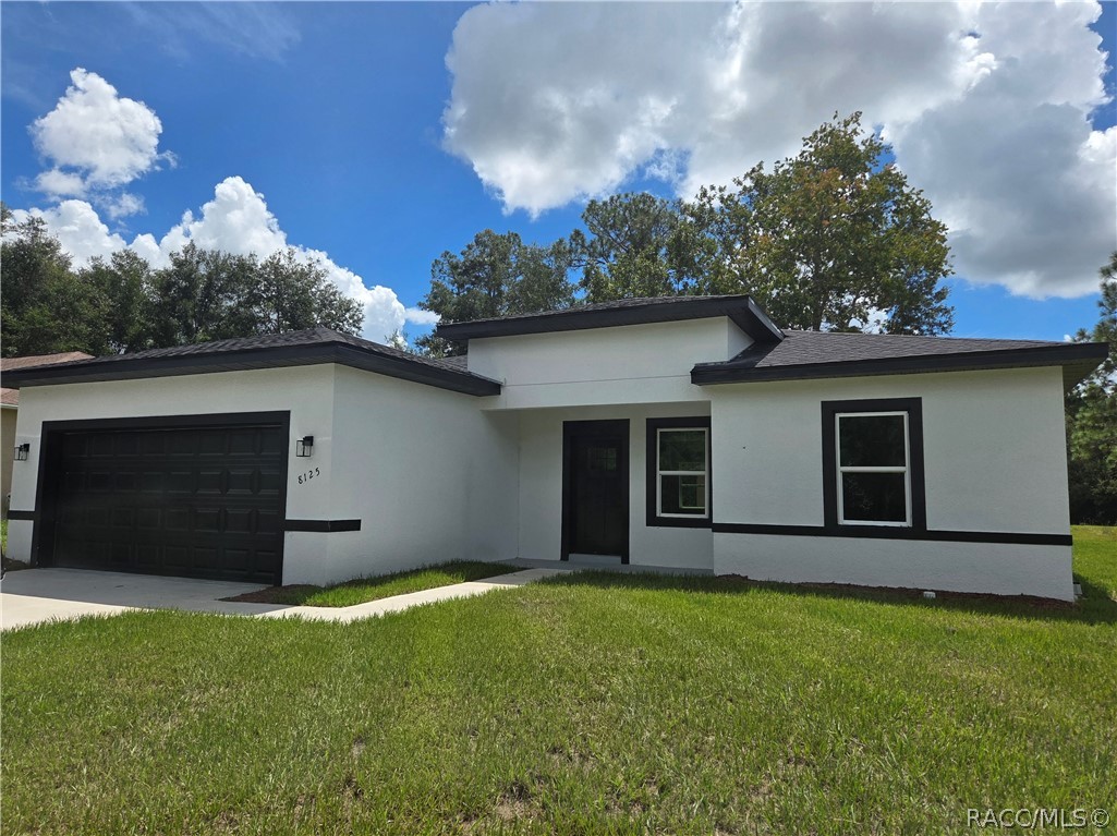 Modern white single-story home with black trim, an attached garage, and a broad green lawn.