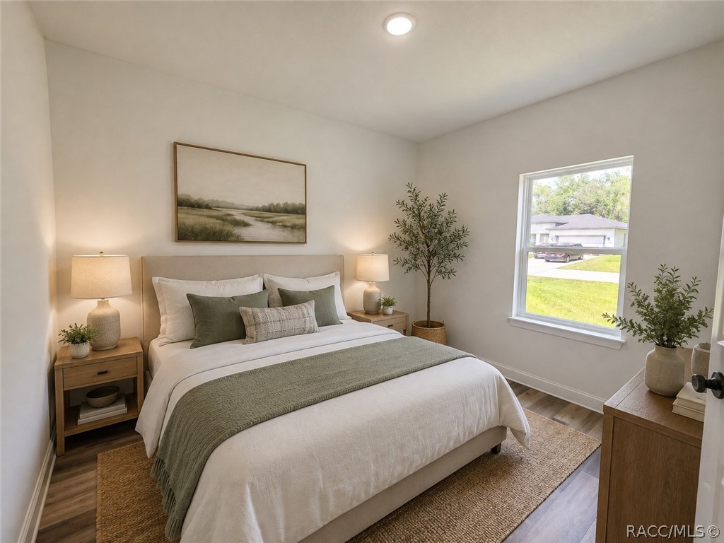 Staged bedroom with a white bed, green throw, wooden nightstands, and a window overlooking the yard.