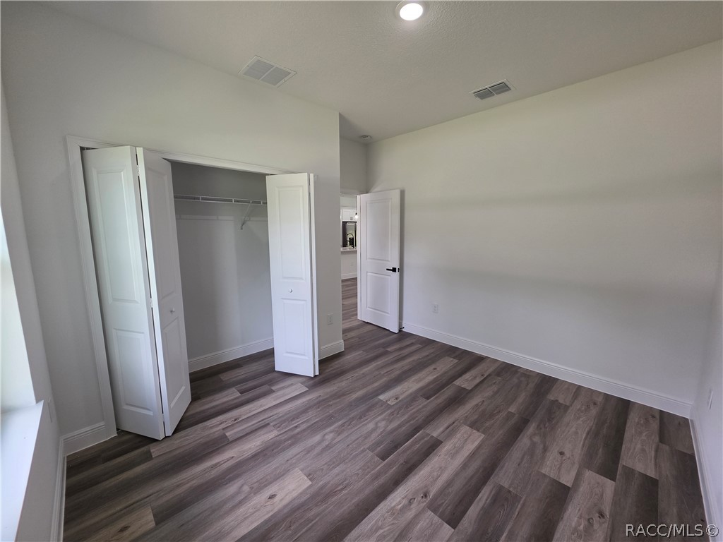 Empty bedroom with an open closet and dark gray wood-look flooring.