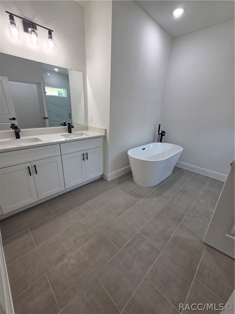 Bathroom with a white double vanity and freestanding soaking tub on gray tile floors.