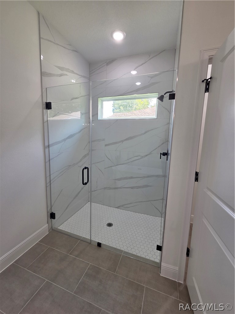 Walk-in shower with glass doors, marble-look tile, hexagonal floor, and a narrow window.