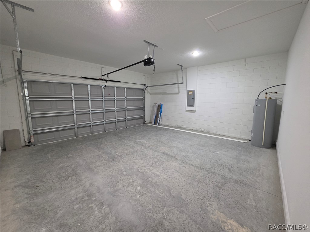 Empty garage with a wide overhead door, concrete floor, and cylindrical water heater.