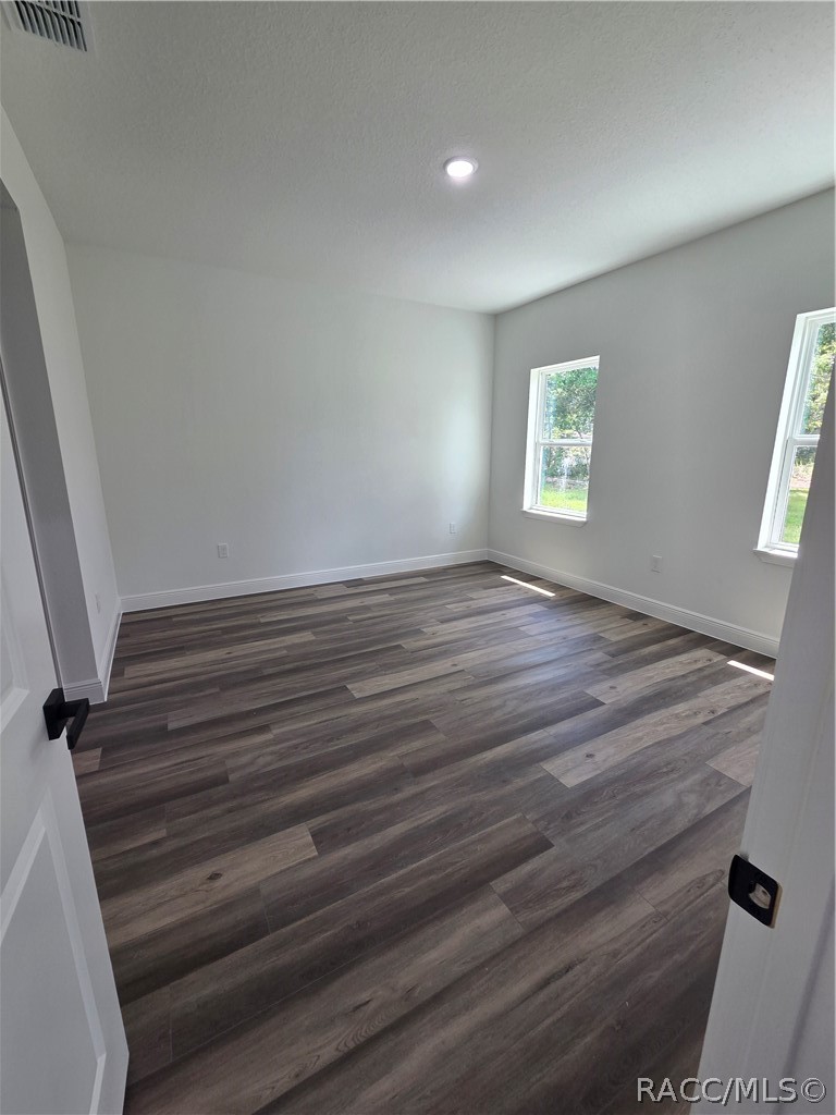 Empty room with dark wood-look plank flooring, gray walls, and two windows.