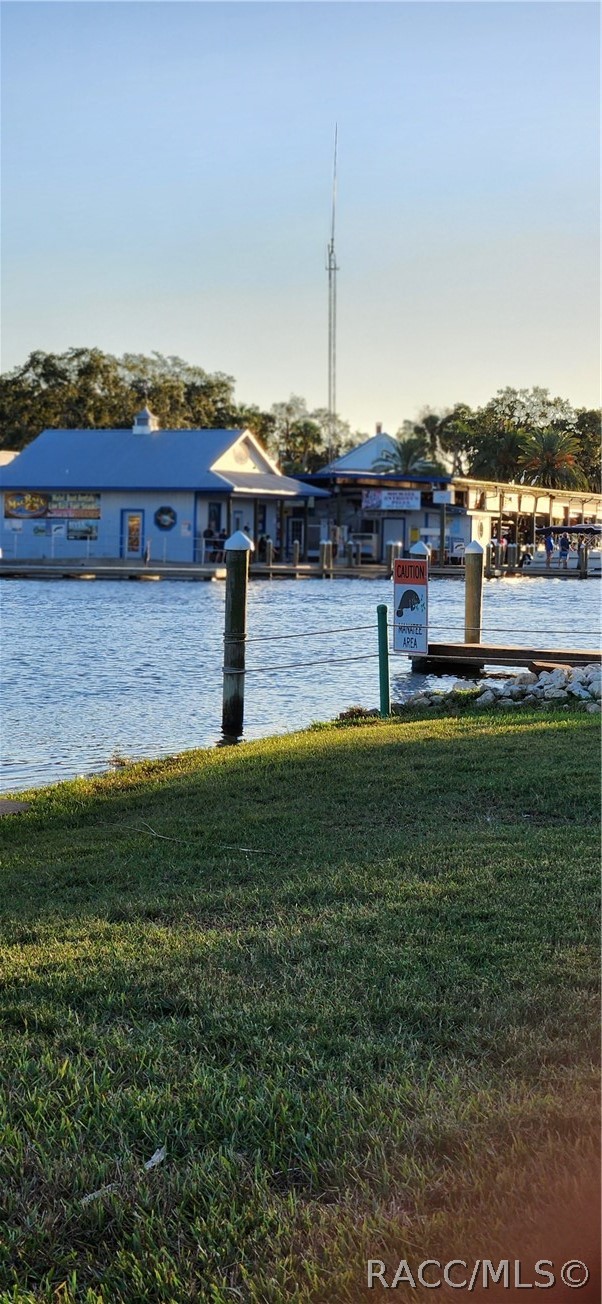 Waterfront marina across calm water, viewed from a grassy bank with dock pilings.