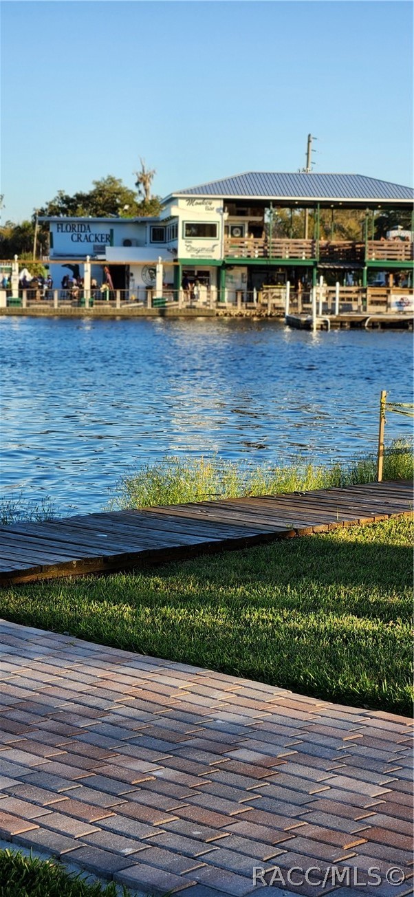 Waterfront view of a restaurant across the water, with docks, a lawn, and paved patio in the foreground.