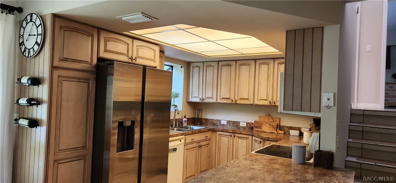 Kitchen with light wood cabinets, stainless steel refrigerator, granite counters, and a cooktop peninsula.