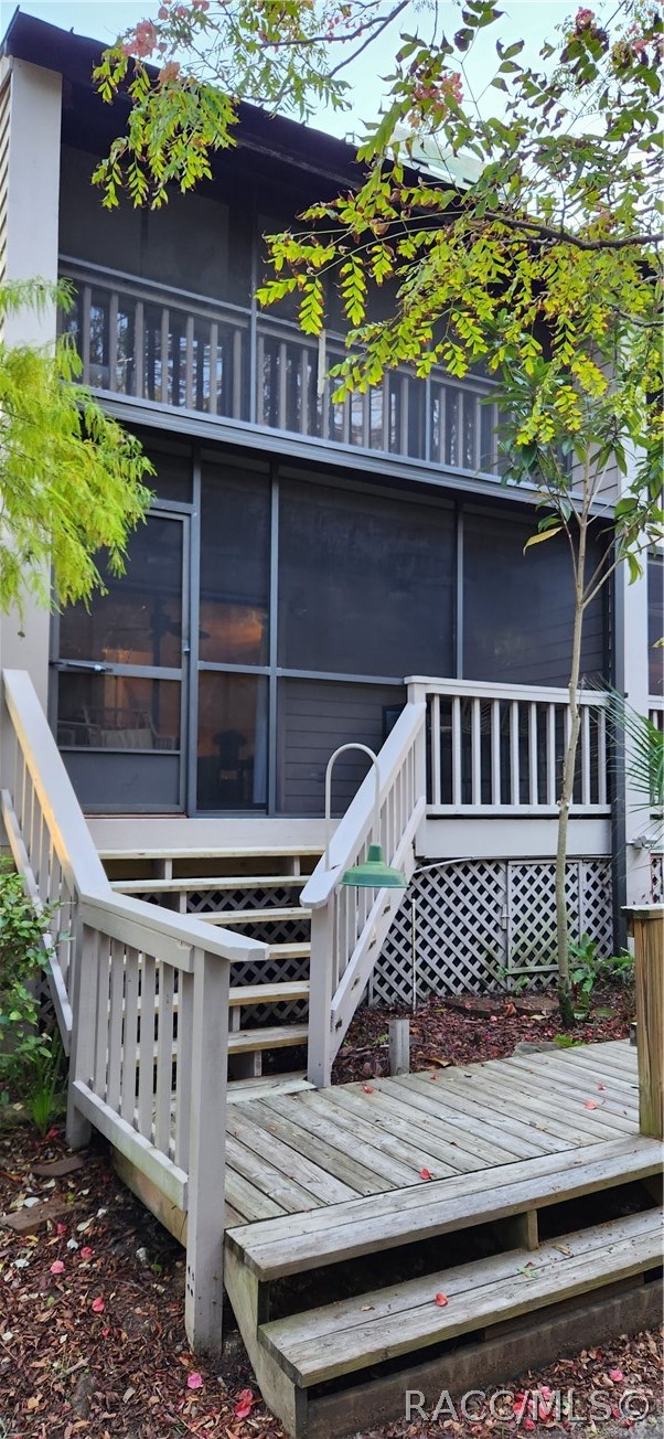 Home exterior with a screened porch and wooden deck, white-railed stairs, and leafy trees.
