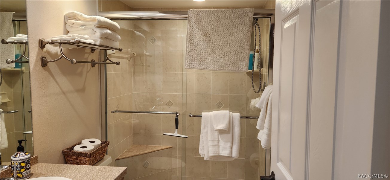 Bathroom with a glass-enclosed tiled shower, corner bench, and white towels.