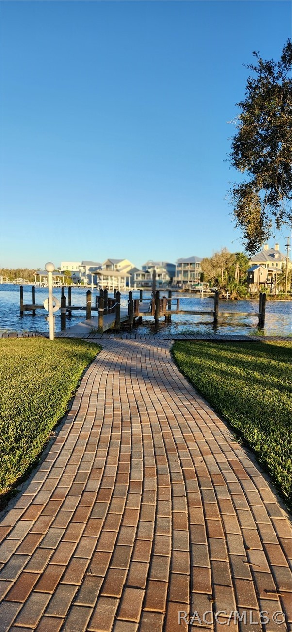 Brick walkway leading to a waterfront dock, with homes across the water.