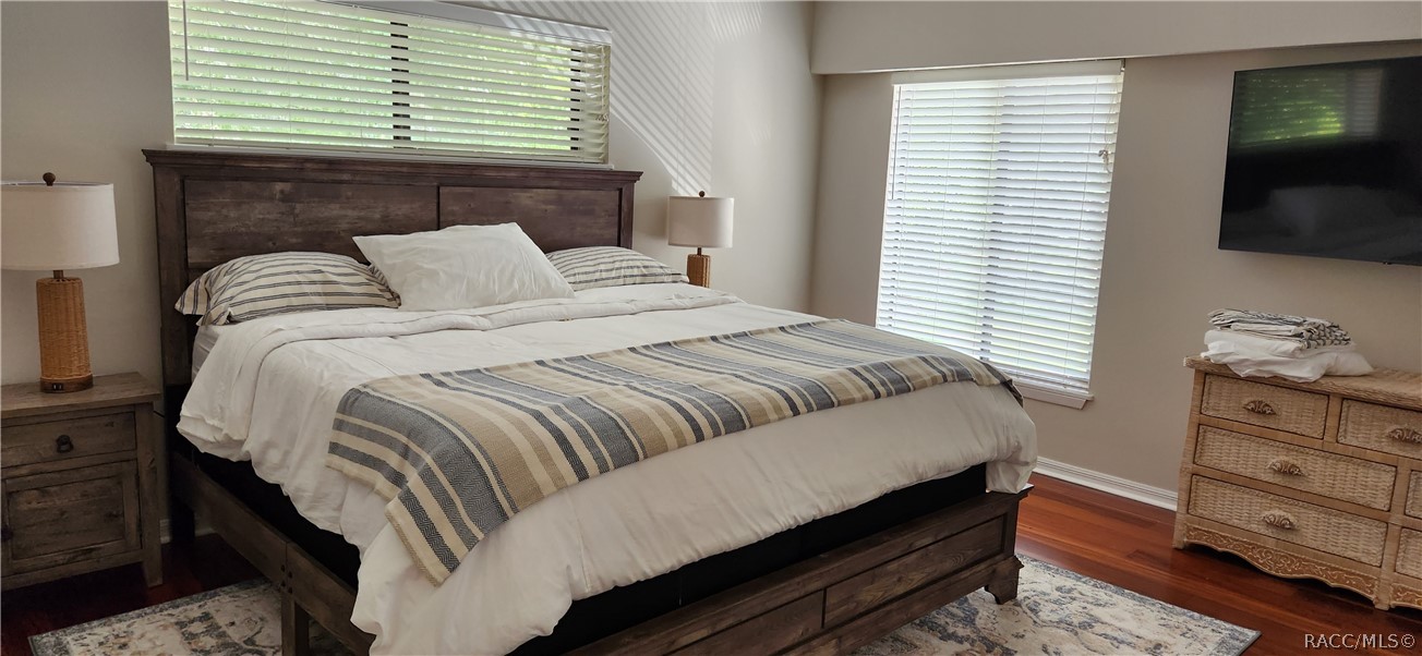 Bedroom with a dark wood bed, white bedding, striped accents, and windows with blinds.