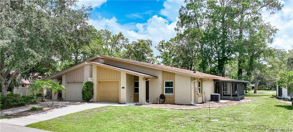 Single-story beige home with an attached garage, screened patio, and mature trees.