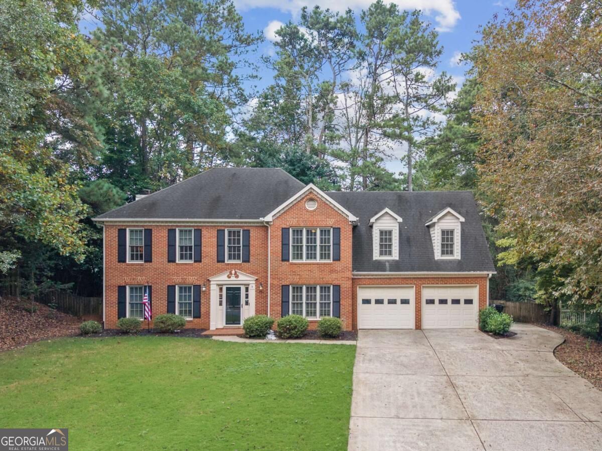 Two-story brick house with black shutters, two dormers, a double garage, and a broad concrete driveway.