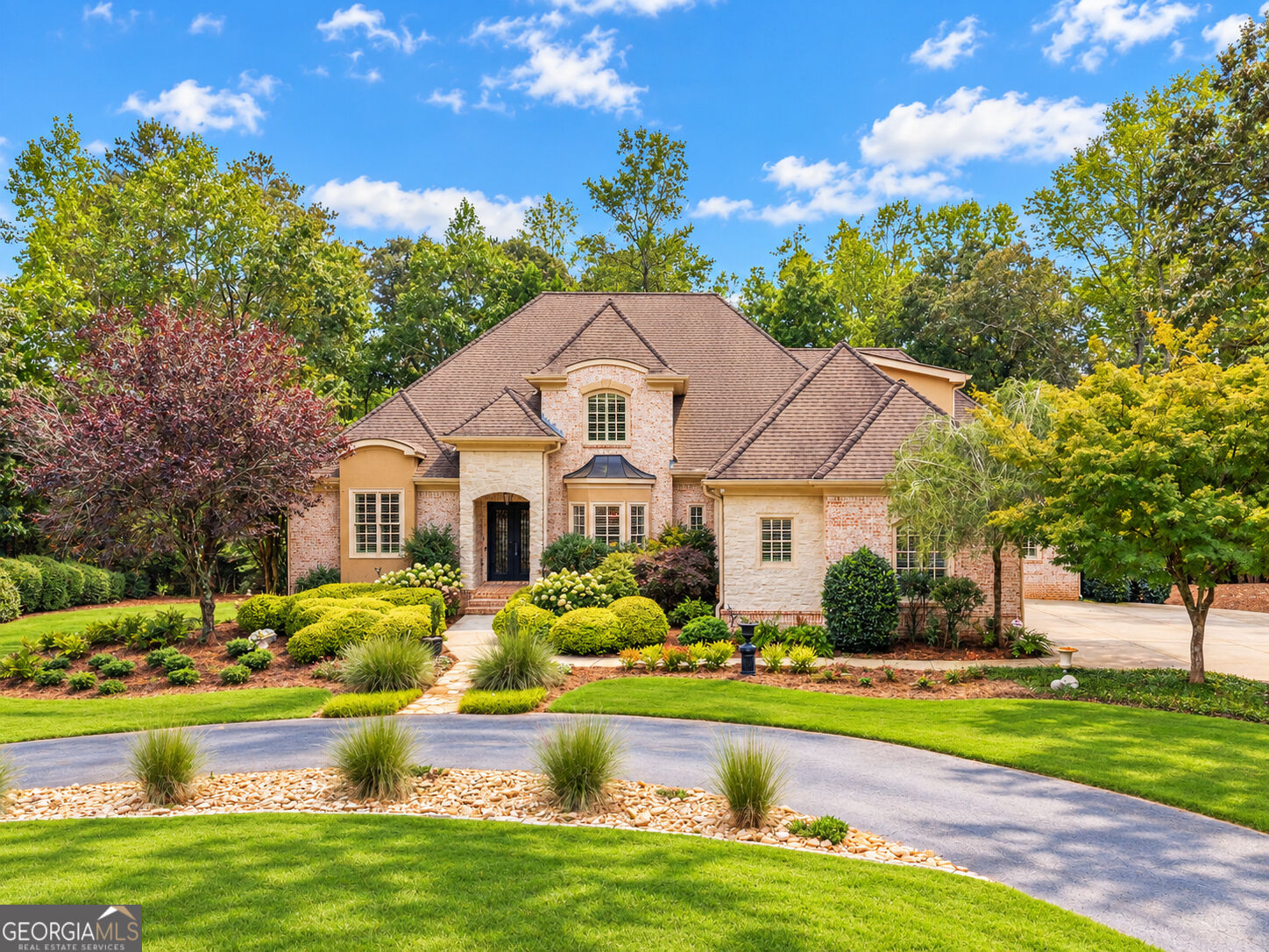 Large stone-and-brick house with a multi-gabled roof, landscaped garden, and curved driveway.