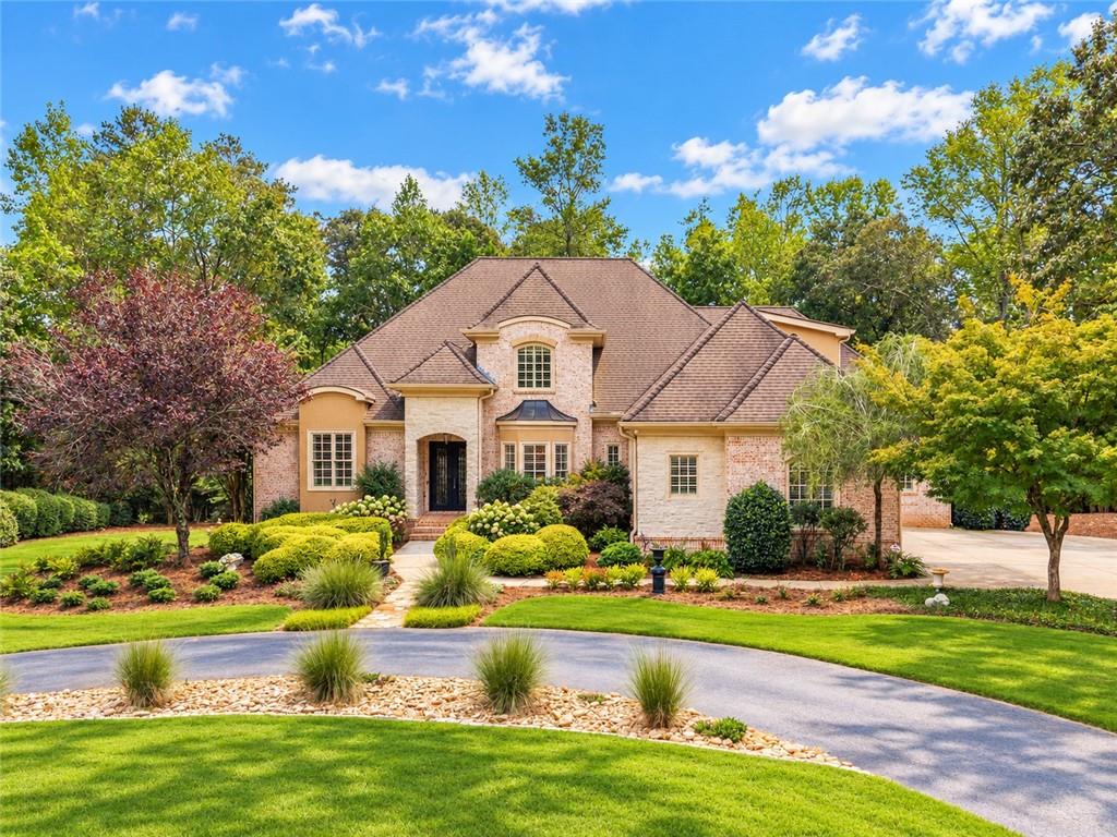 Brick house with a steep gabled roof, landscaped gardens, mature trees, and a curved driveway.