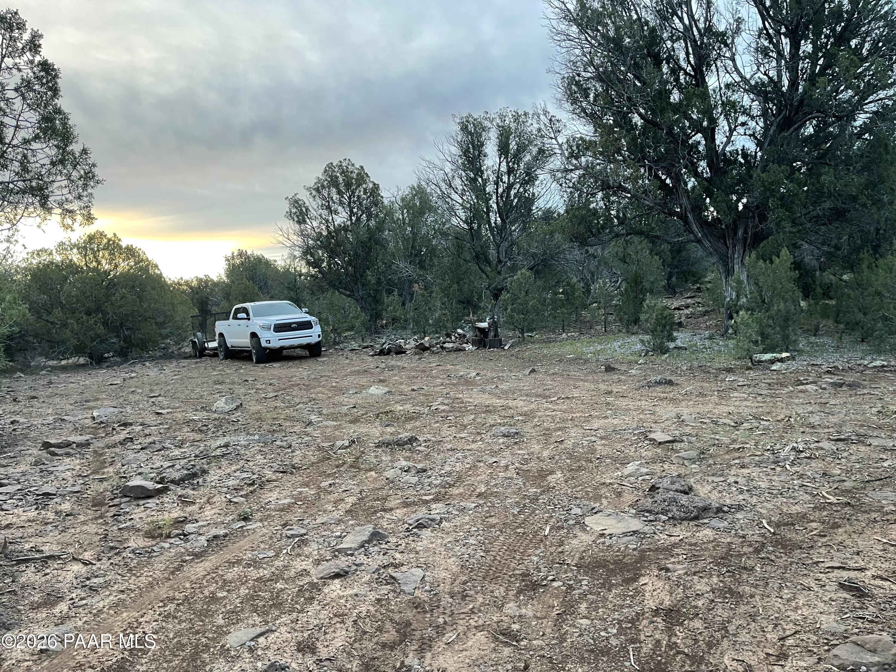 Rocky wooded lot with a white pickup parked in a clearing beneath a glowing evening sky.