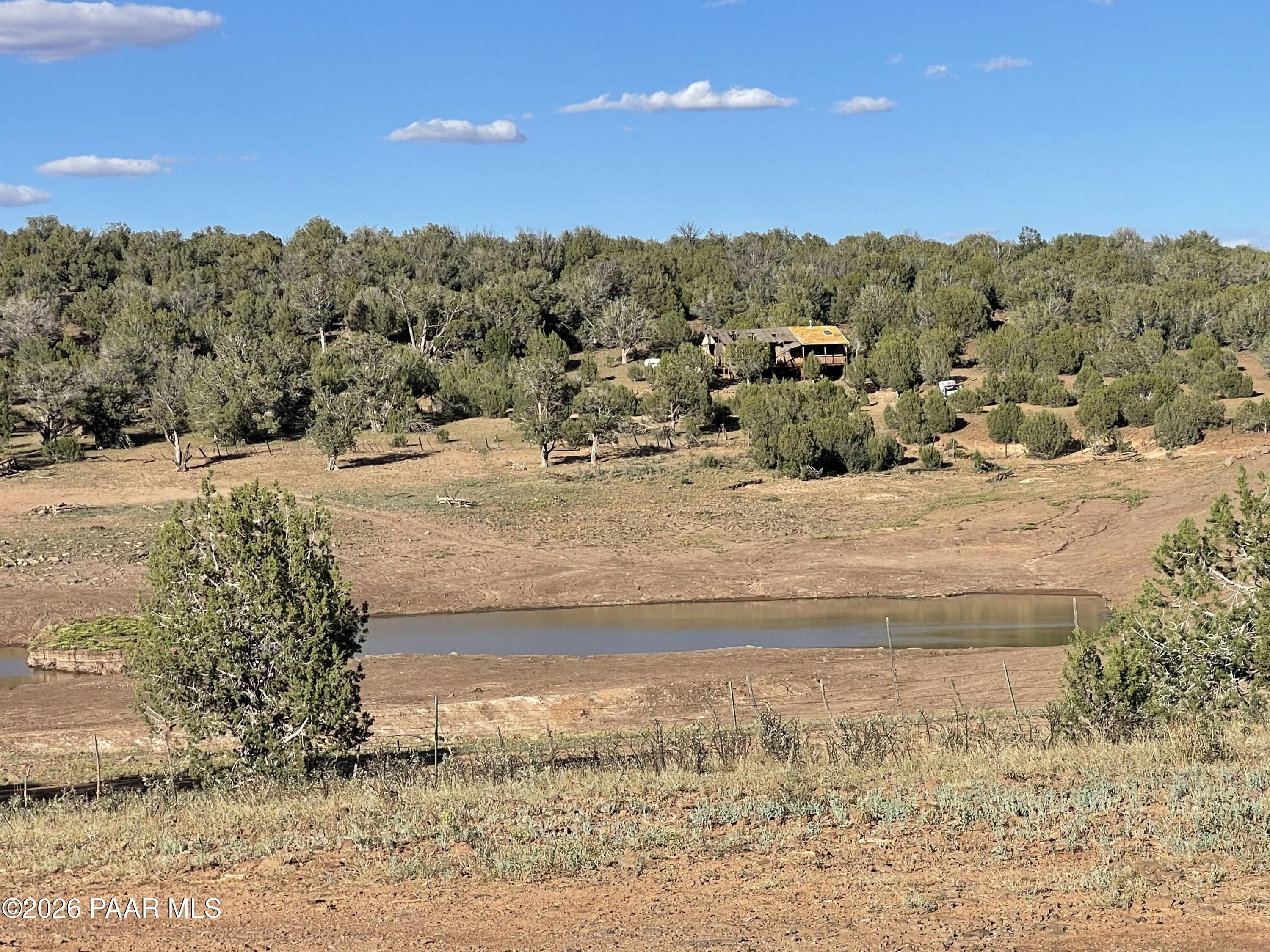 Rural property with a pond, open dry ground, and a cabin among scattered trees.