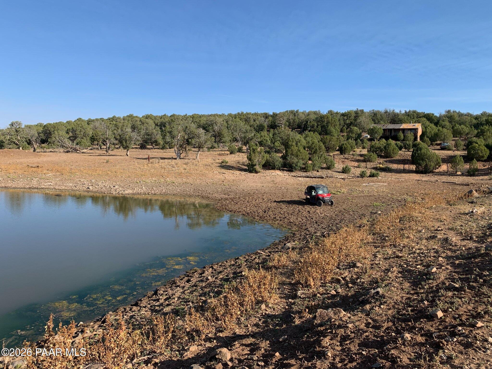 Rocky rural land with a pond, scattered trees, and a red utility vehicle.