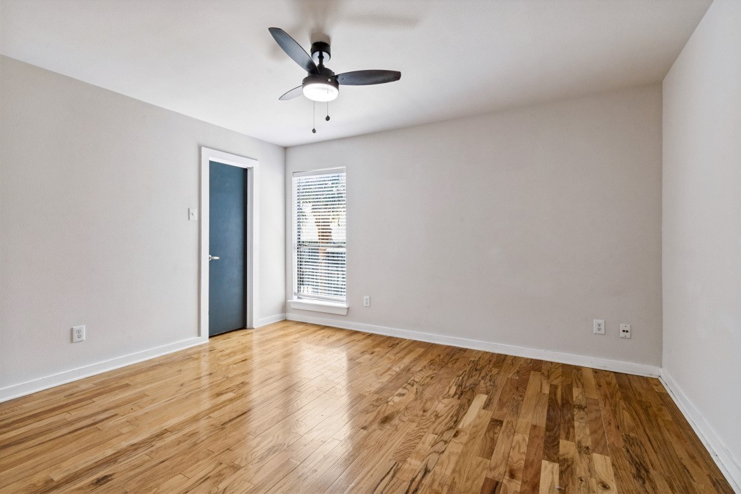 Empty room with hardwood floors, a ceiling fan, and a window with blinds.