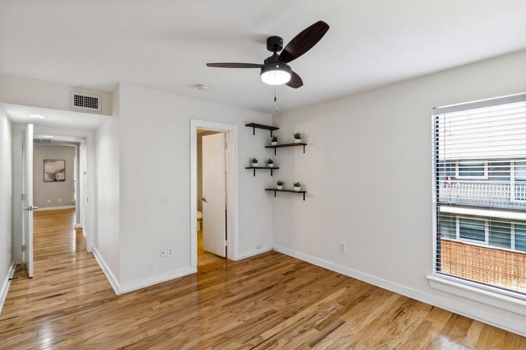 Unfurnished condo room with hardwood floors, a ceiling fan, plant shelves, and a large window.