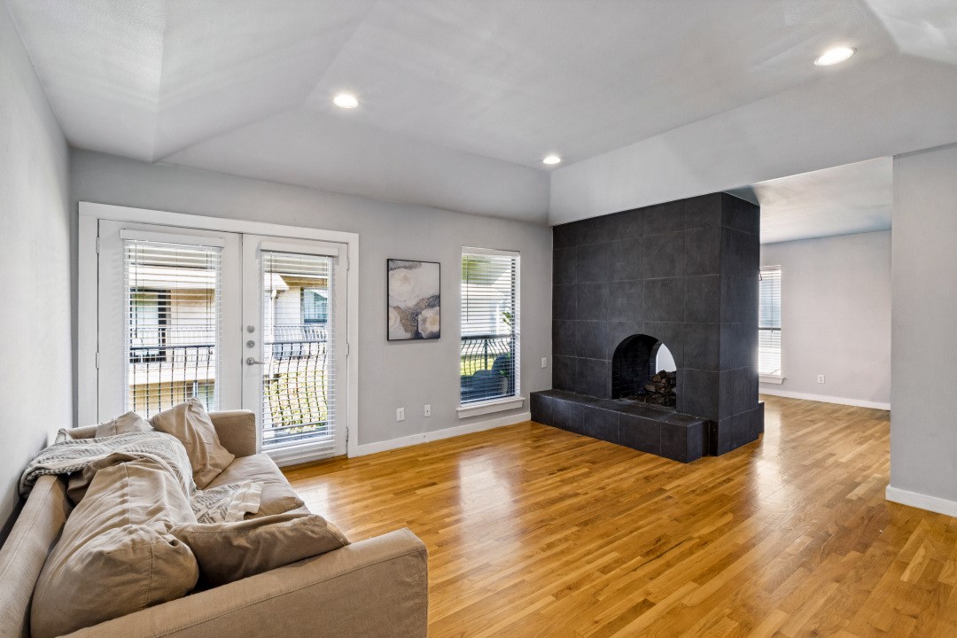 Living room with a beige sofa, hardwood floors, and a large dark tiled fireplace.