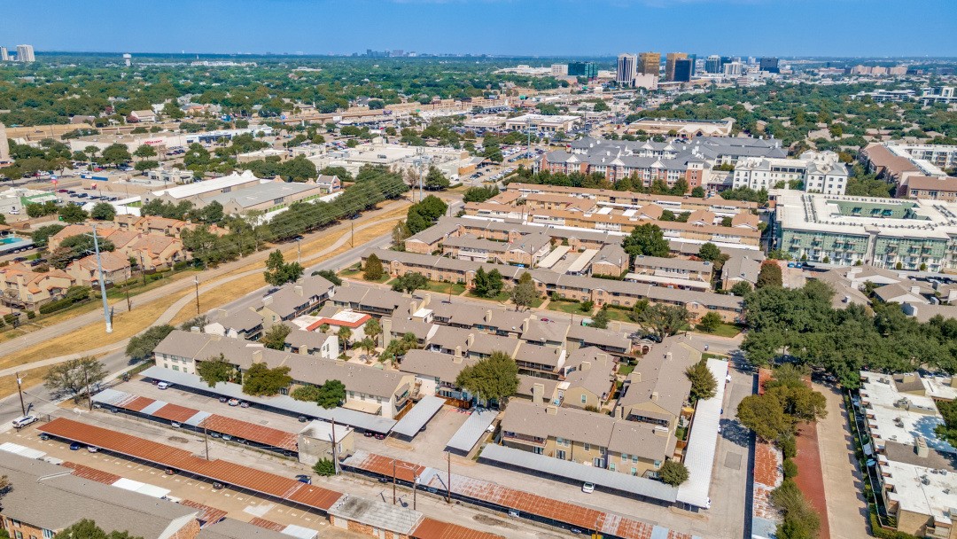 Aerial view of low-rise apartments and tree-lined streets with the Dallas skyline in the distance.