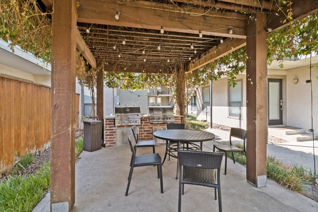 Patio beneath a vine-covered pergola with string lights, grills, and outdoor dining furniture.