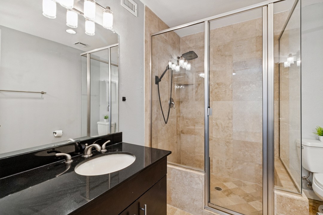 Bathroom with a black vanity and beige-tiled glass shower.