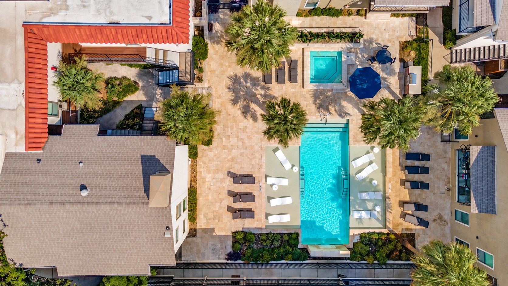 Aerial condominium courtyard with a long pool, spa, palms, and lounge seating.