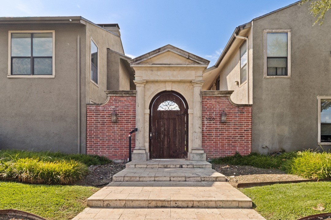 Residential building entrance with a stone arch, wooden gate, brick wall, and paved front walkway.