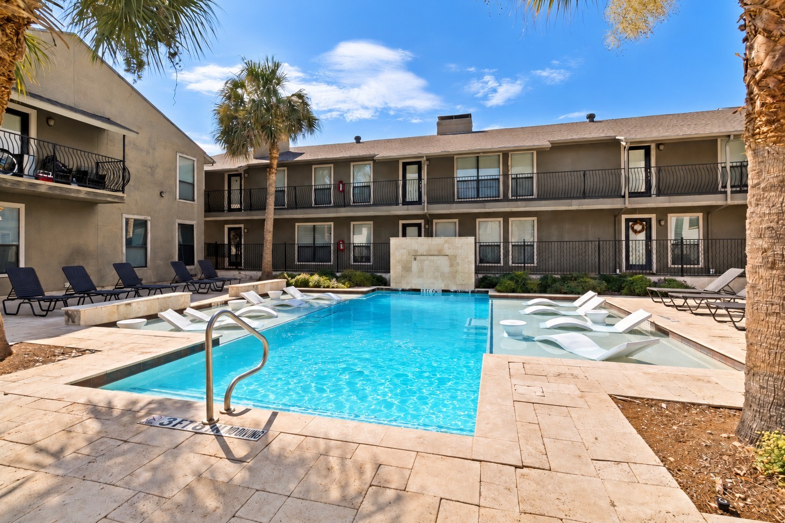 Courtyard pool with submerged loungers, deck chairs, and palm trees.