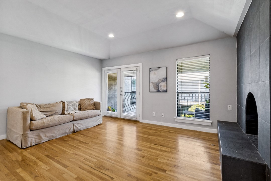 Living room with hardwood floors, a beige sofa, and a dark tiled fireplace.