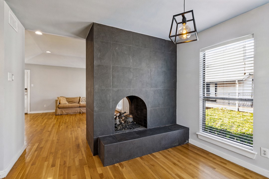 Living room with a tall dark-tiled fireplace, hardwood floors, and a window with white blinds.