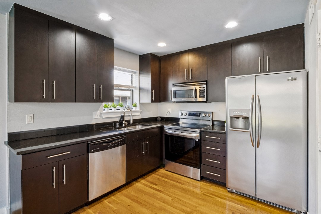 Kitchen with dark wood cabinets, black countertops, stainless steel appliances, and hardwood floors.
