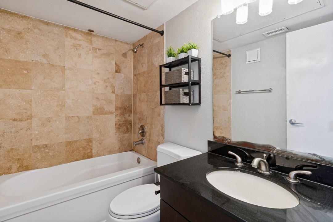 Bathroom with a tan tile tub surround, black vanity countertop, oval sink, and wall shelf with plants.