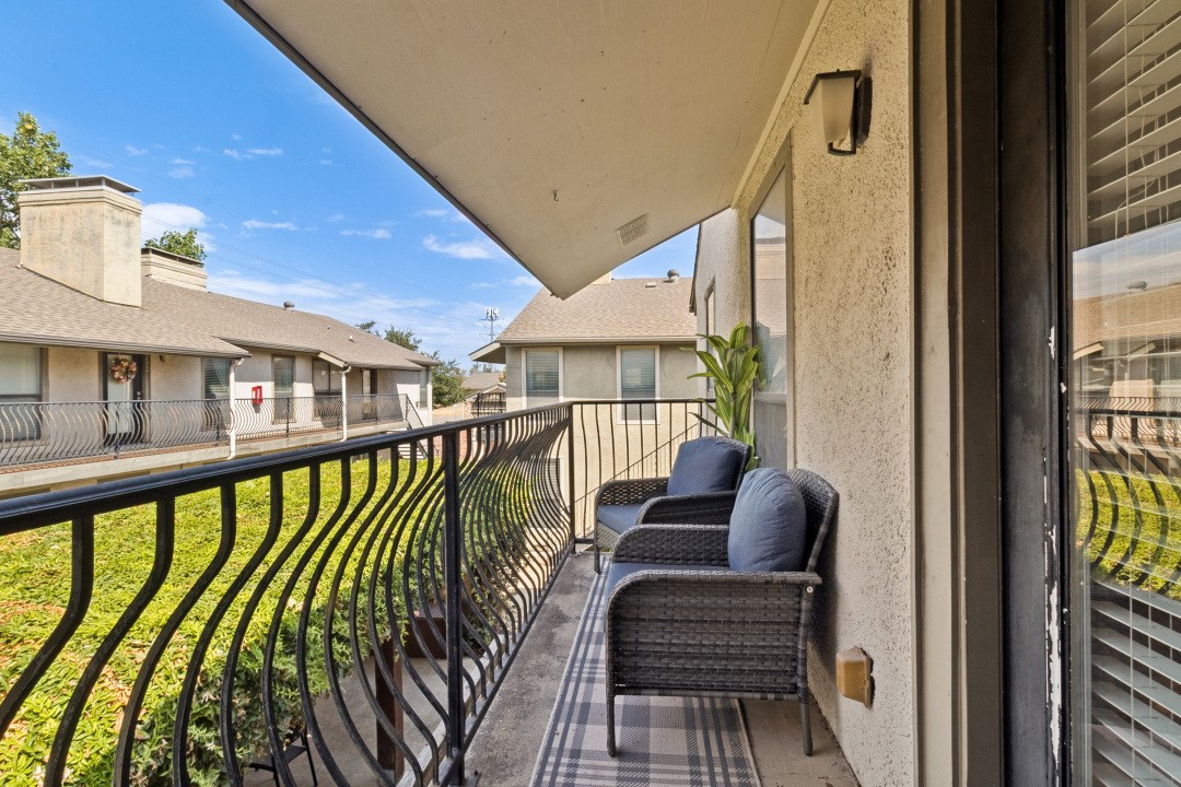 Apartment balcony with wicker chairs, blue cushions, and a view of neighboring buildings.