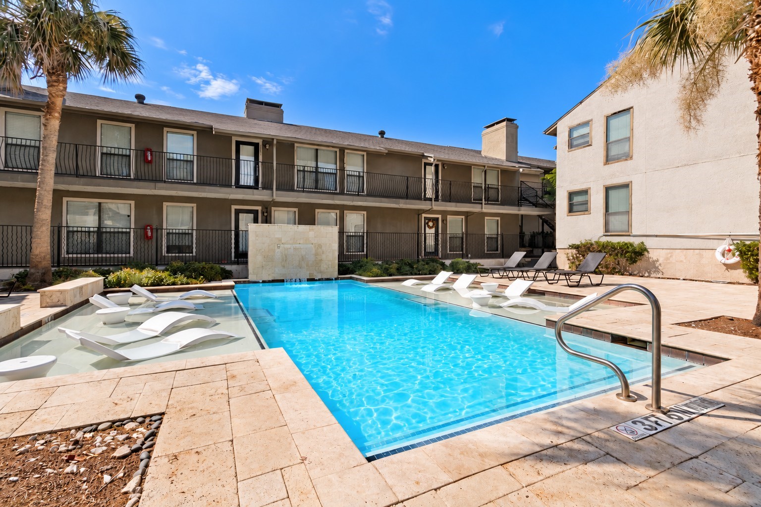 Apartment courtyard pool with a shallow tanning ledge and white in-water loungers.