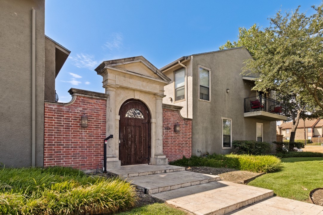 Condominium entrance with a stone arch, wooden gate, red brick wall, and second-floor balcony.