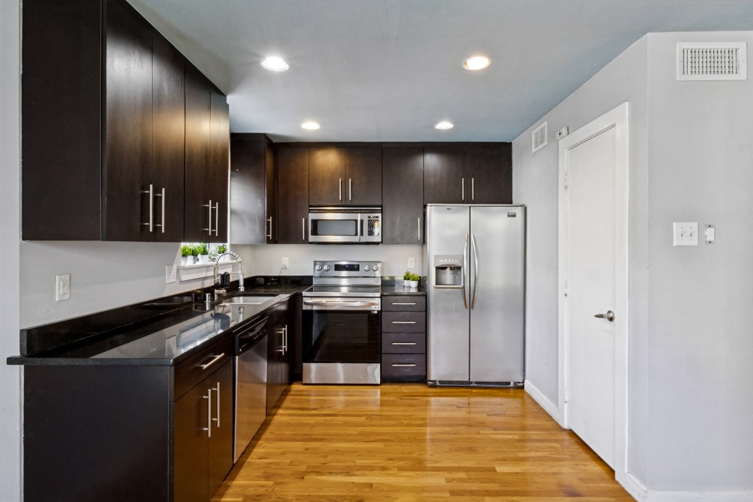 Kitchen with dark wood cabinets, black countertops, stainless steel appliances, and hardwood floors.