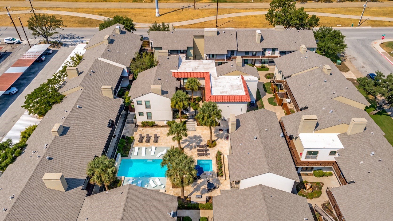 Aerial view of a condominium complex surrounding a palm-lined courtyard and swimming pool.