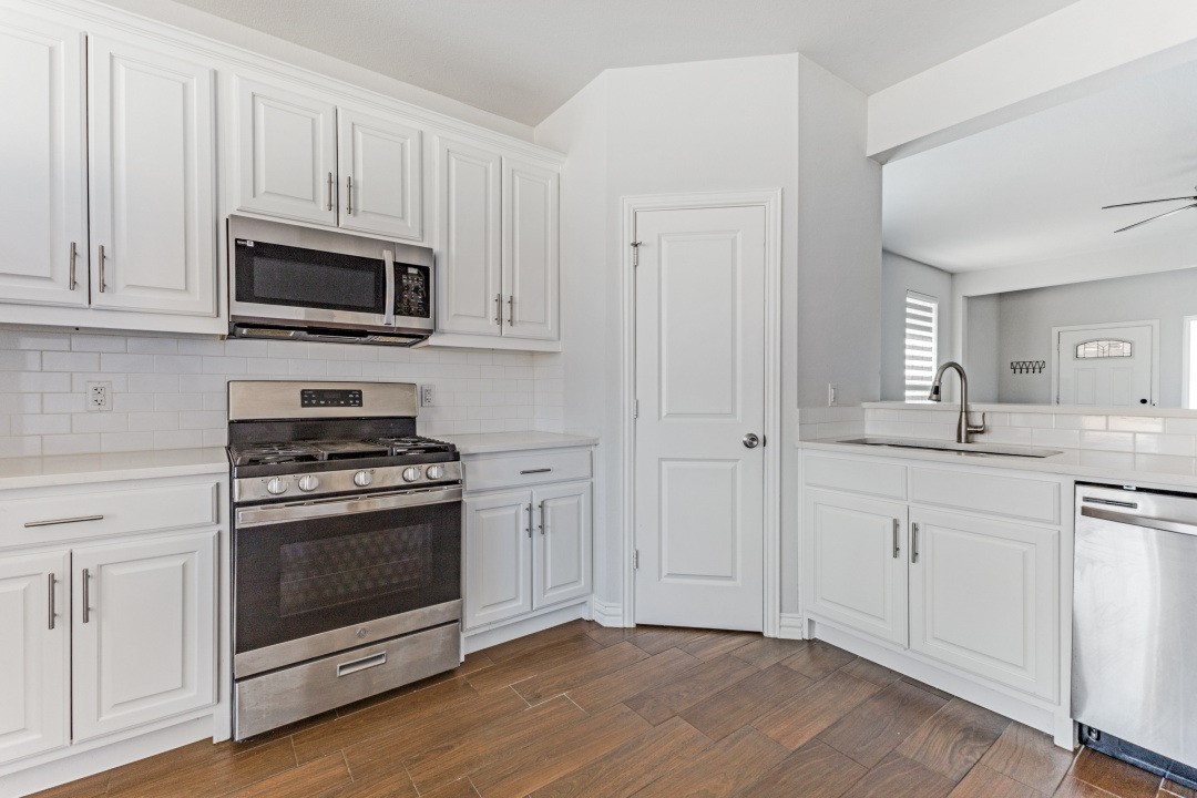 White kitchen with paneled cabinets, stainless steel appliances, and brown wood-look flooring.
