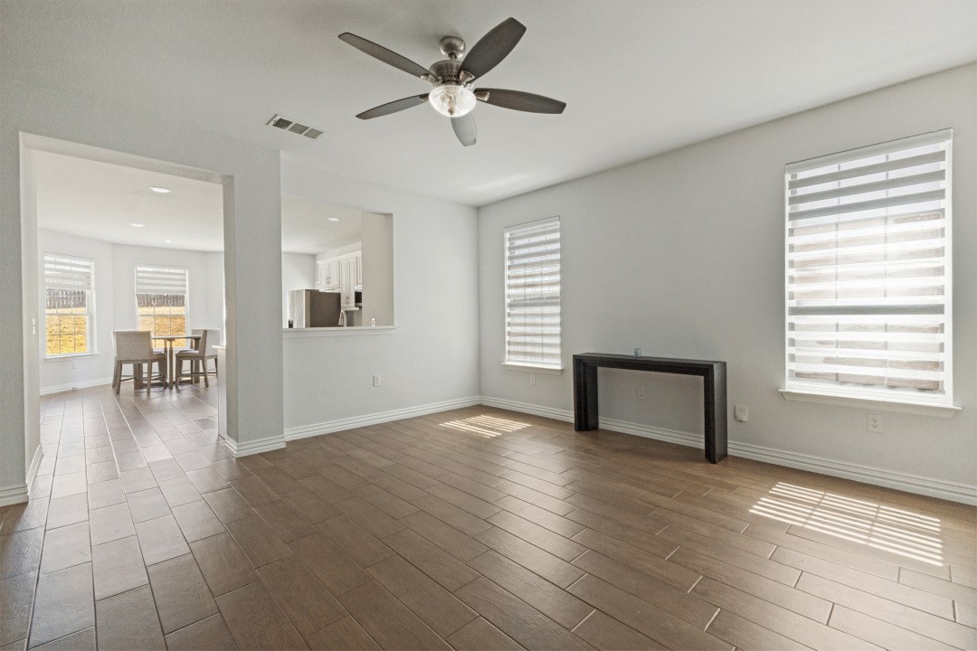 Living room with plank-style tile flooring, ceiling fan, large windows, and an adjoining dining area.